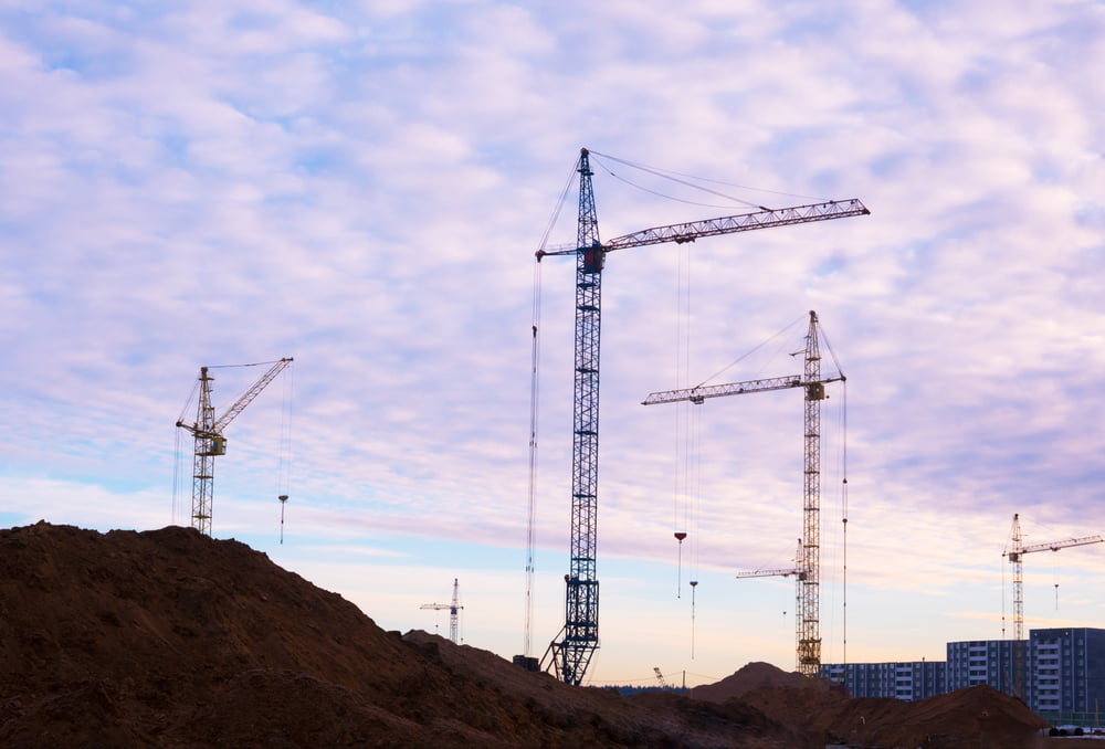 A construction site with cranes set against a dusky sky