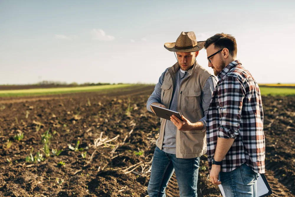 Two men in a recently ploughed paddock discuss how to connect and monitor their IoT devices