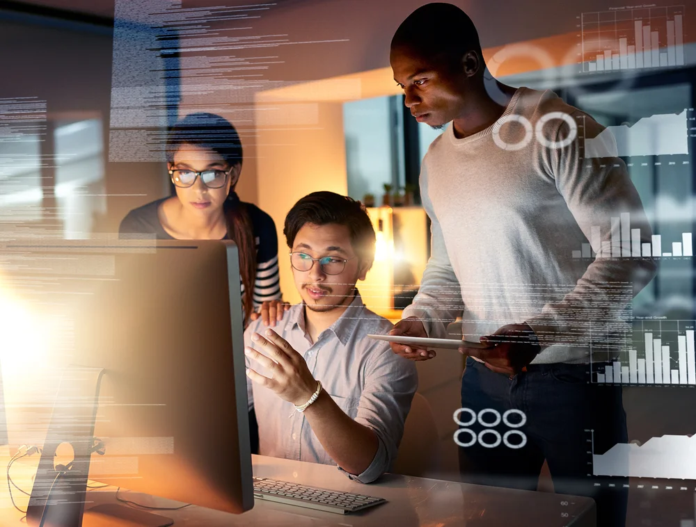 Three colleagues huddled around a computer conduct IoT device monitoring and data assessment